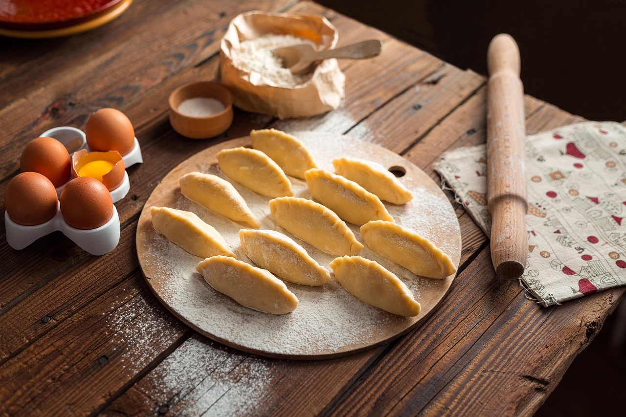Surowe pierogi oprószone mąką na stolnicy położonej na drewnianym stole.